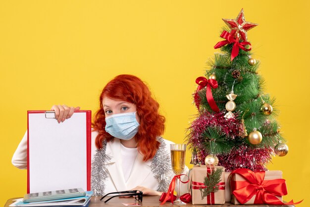 크리스마스 트리와 마스크에 앉아 선물 주위 전면보기 여성 의사