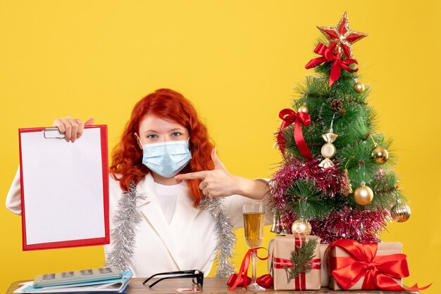 Вид спереди женщина-врач вокруг елки и подарки, сидя в маске