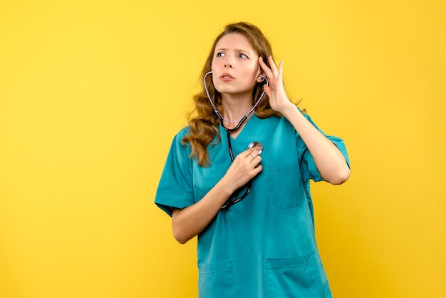 Front view female doctor checking heartbeats on yellow space