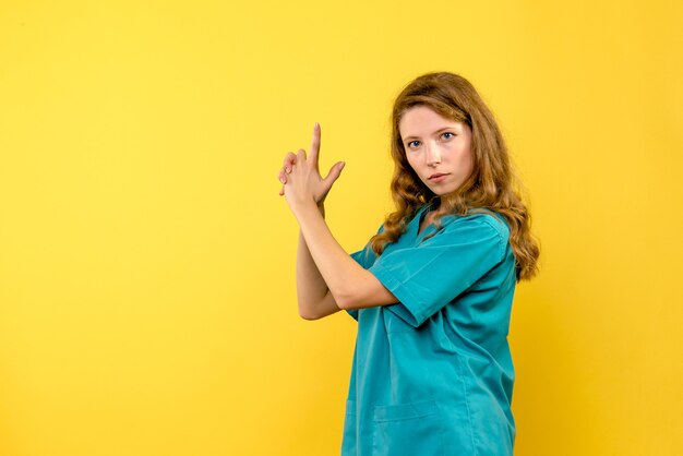 Вид спереди женщина-врач в позе, держащей пистолет на желтом пространстве
