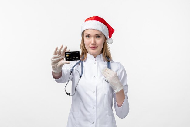 Front view of female doctor holding bank card on a white wall