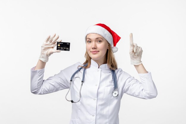 Front view of female doctor holding bank card on white wall