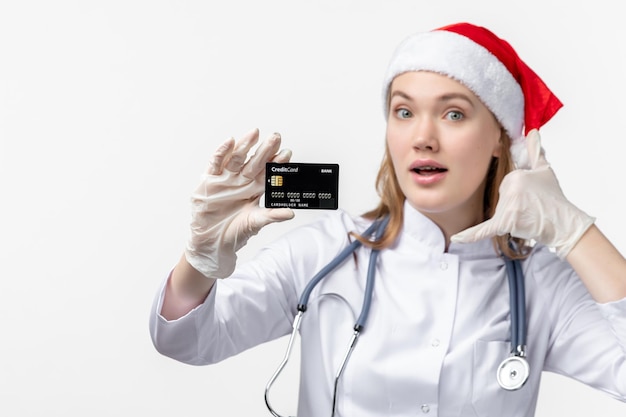 Front view of female doctor holding bank card on white wall