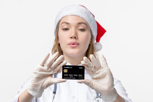 Front view of female doctor holding bank card on white wall