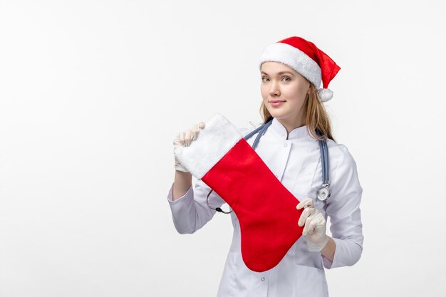 Vista frontale della dottoressa che tiene un grande calzino natalizio sul muro bianco