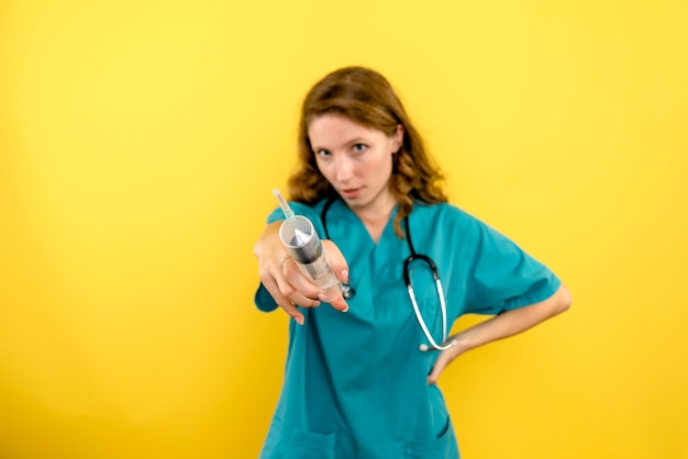 Front view female doctor holding big injection on a yellow space