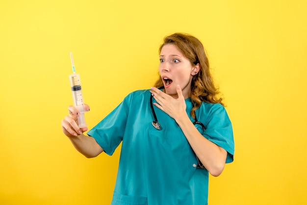 Front view female doctor holding big injection on a yellow space