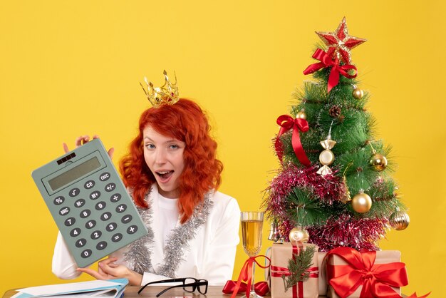 Front view female doctor holding calculator around xmas presents and tree