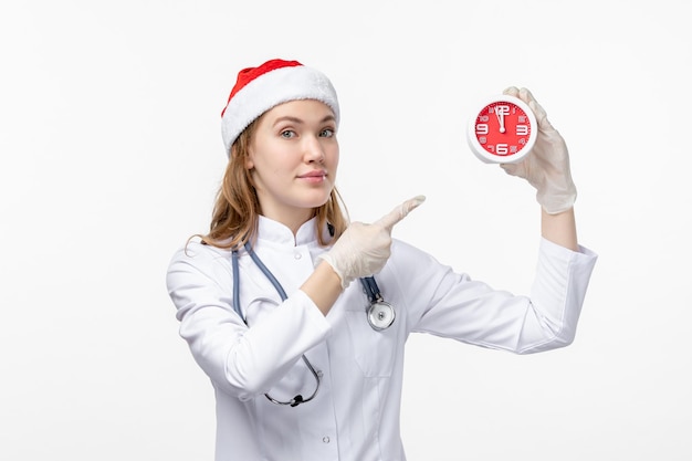 Front view of female doctor holding clock on the white wall