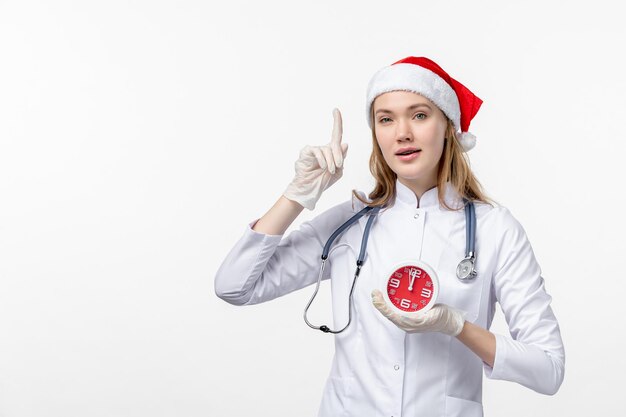 Front view of female doctor holding clock on the white wall