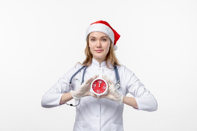 Vista frontale della dottoressa che tiene l'orologio sul muro bianco