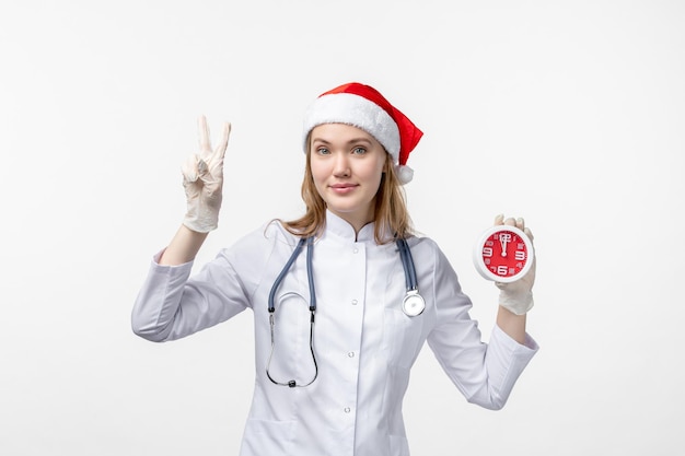 Front view of female doctor holding clock on white wall