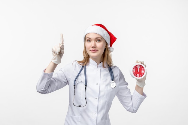 Front view of female doctor holding clock on white wall