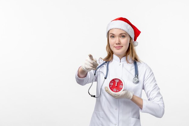 Front view of female doctor holding clock on white wall