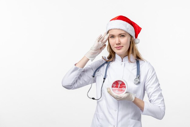 Front view of female doctor holding clock on white wall