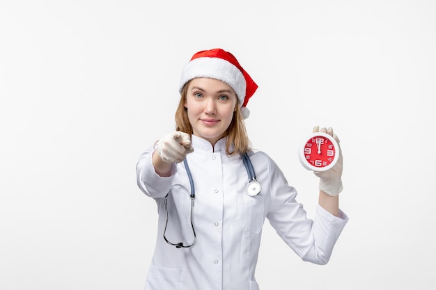 Front view of female doctor holding clock on white wall