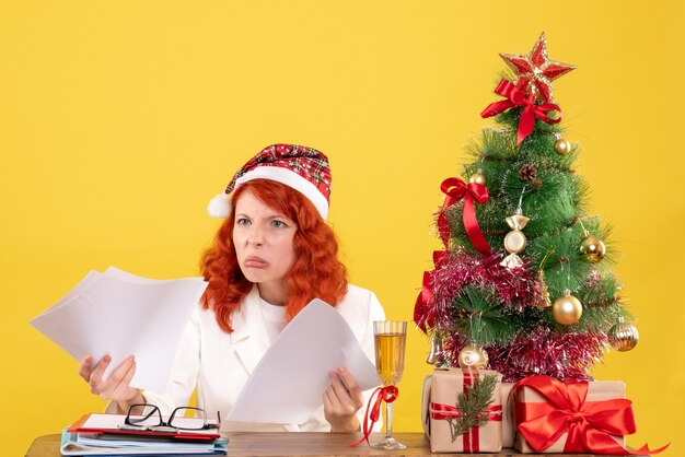 Вид спереди женщина-врач держит документы и сидит с рождественскими подарками