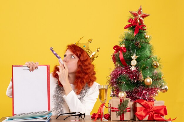 Вид спереди женщина-врач, держащая файл заметки вокруг рождественской елки и подарков