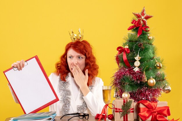 Front view female doctor holding file note around xmas tree and presents