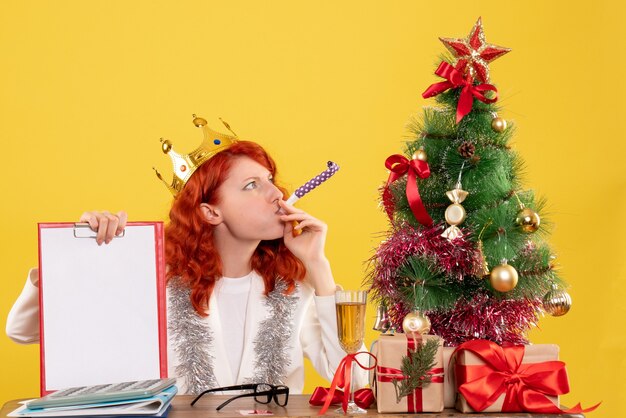 Front view female doctor holding file note around xmas tree and presents