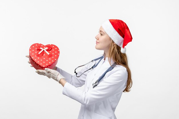 Front view of female doctor holding holiday present on a white wall