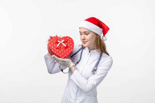 Front view of female doctor holding holiday present on a white wall