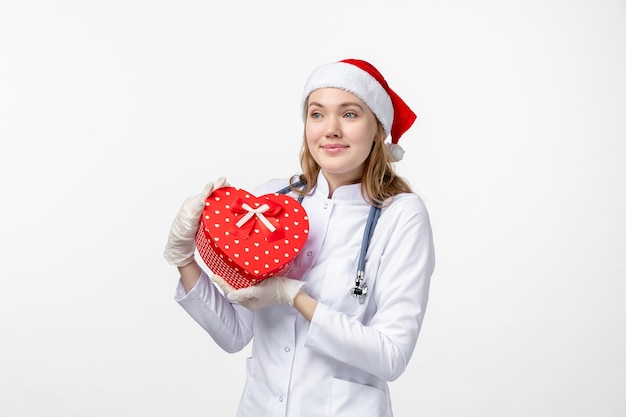 Front view of female doctor holding holiday present on white wall