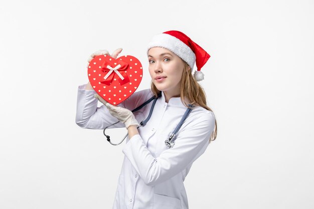 Front view of female doctor holding holiday present on white wall