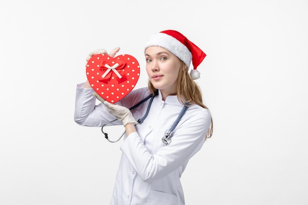 Front view of female doctor holding holiday present on white wall