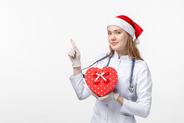 Front view of female doctor holding holiday present on white wall