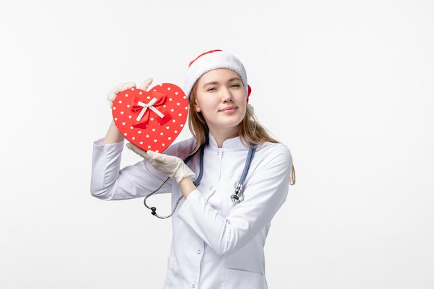 Front view of female doctor holding holiday present on white wall