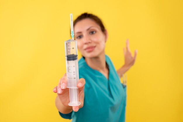 Front view female doctor holding huge injection on yellow background