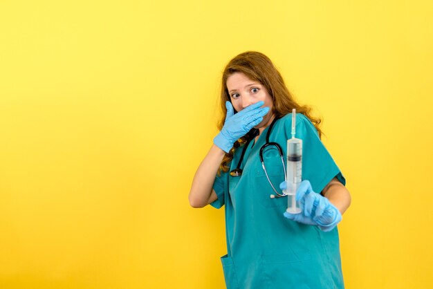 Front view female doctor holding huge injection on a yellow space