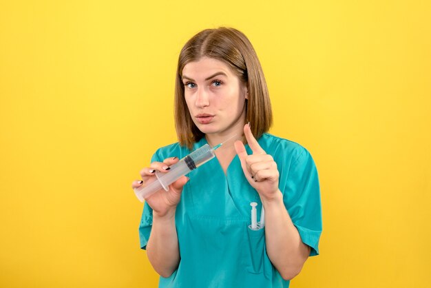 Front view female doctor holding huge injection on a yellow space