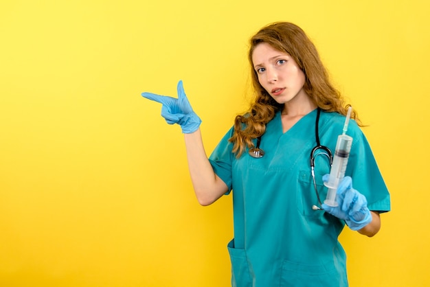 Front view female doctor holding huge injection on the yellow space