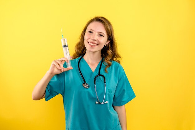 Вид спереди женщина-врач, держащая инъекцию на желтом пространстве
