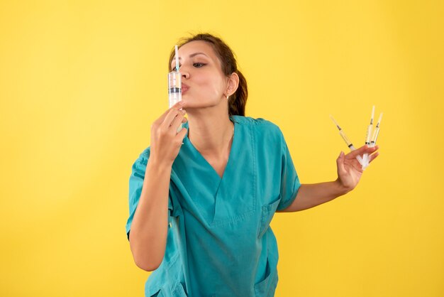 Front view female doctor holding injections on the yellow background