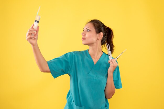 Front view female doctor holding injections on yellow desk hospital illness color medic virus nurse health