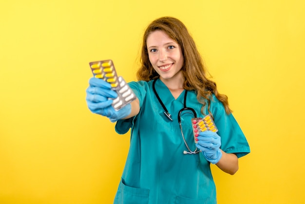 Front view female doctor holding pills on a yellow space