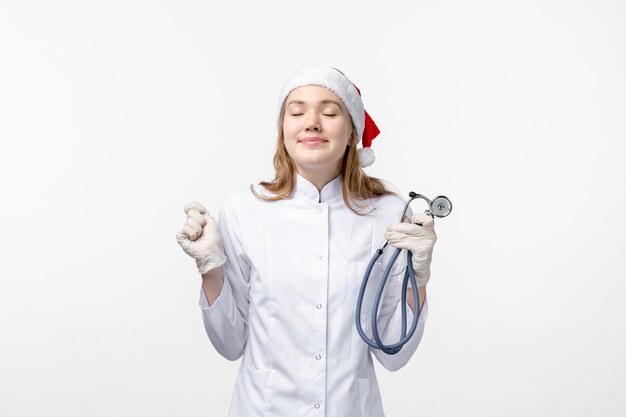 Front view of female doctor holding stethoscope on a white wall