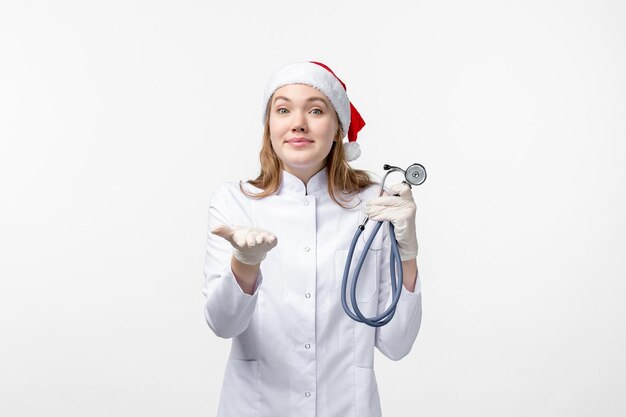 Вид спереди женщина-врач, держащая стетоскоп на белой стене