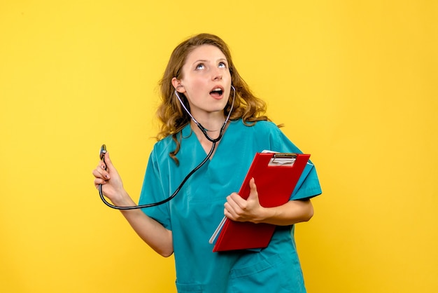 Front view female doctor holding stethoscope on yellow space