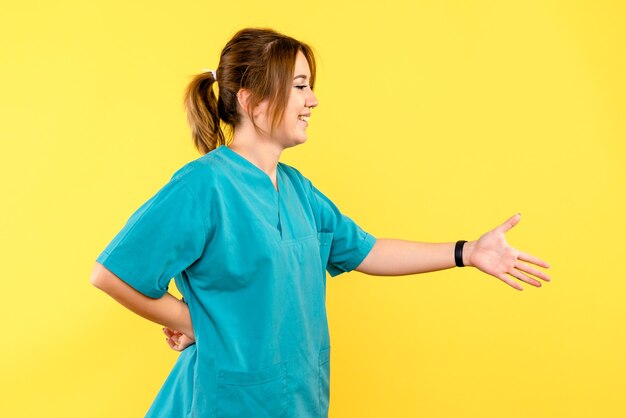 Вид спереди женщина-врач, имитирующая рукопожатие на желтом пространстве