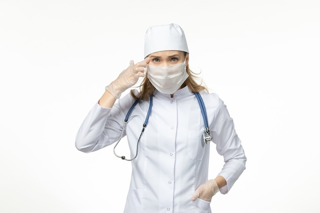 무료 사진 밝은 흰색 벽 질병 유행성 코로나 바이러스로 인해 마스크와 장갑으로 의료 소송에서 전면보기 여성 의사-