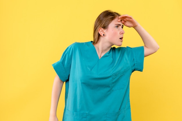 Medico femminile vista frontale guardando a distanza su sfondo giallo salute emozioni ospedale medico