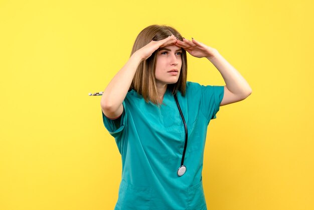 Front view female doctor looking at distance on yellow space