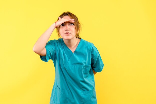 Front view female doctor looking at distance on yellow space