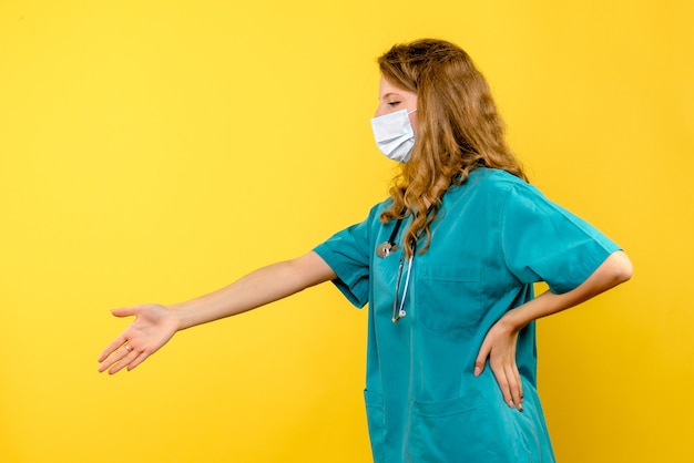 Front view female doctor in mask shaking hands on yellow space