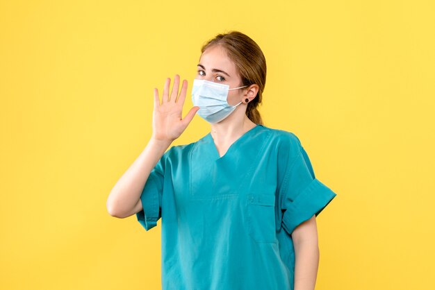 Front view female doctor in mask waving on yellow background pandemic covid- health virus