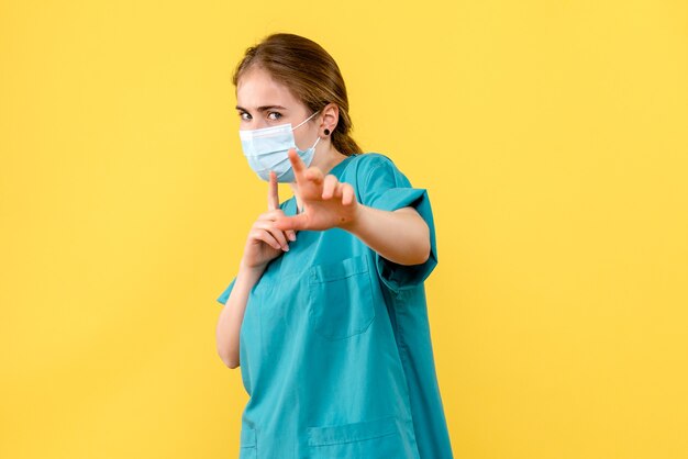 黄色の背景の健康病院covidパンデミックのマスクで正面図の女性医師